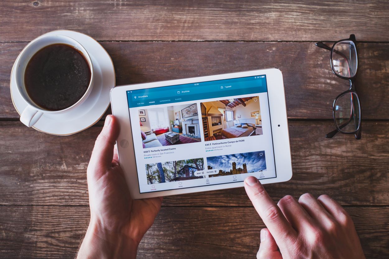 A person browses airbnb on their tablet, with a cup of coffee in the background.